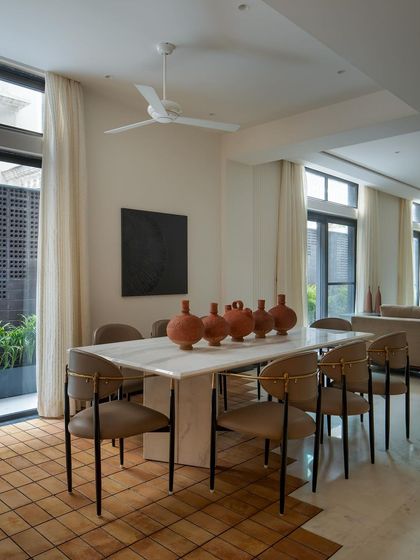 The dining area is anchored by a white marble table and terracotta vessels, continuing the narrative of rugged and refined. Abundant natural light creates a bright, airy atmosphere.