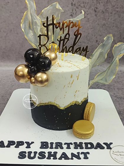 A classy black and gold birthday cake with macarons and translucent sails. This modern design is perfect for a sophisticated milestone celebration.