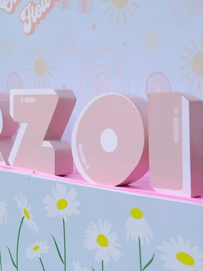 A personalized 3D name sign for "Arzoie" at her sunshine-themed party. The base is decorated with a daisy pattern, tying into the overall floral and sunny vibe.