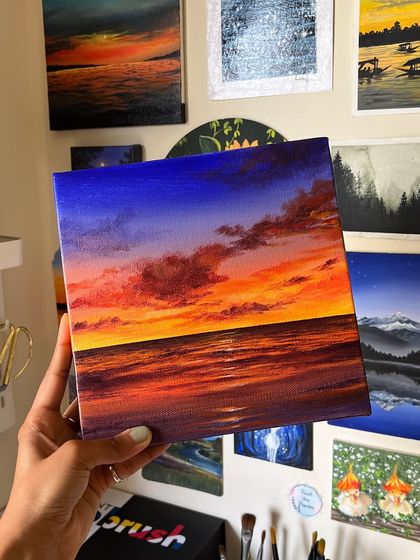 Holding the finished vibrant sunset painting in my studio, showing it against the backdrop of my other creations.