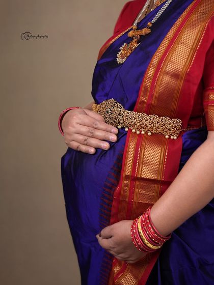 A close-up shot focusing on the baby bump, adorned with a traditional waistband (vaddanam) over a beautiful blue silk saree.