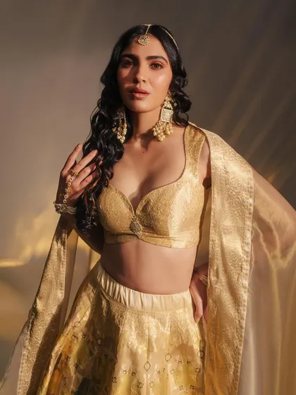 A close-up of a gorgeous golden Benarasi lehenga. The intricate weave and the pairing with traditional pearl and polki jewelry create a look of timeless elegance.