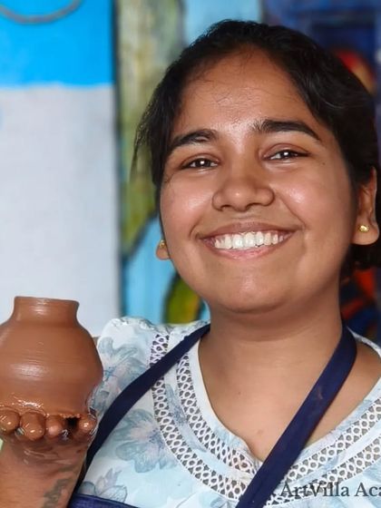 A student shows off the small pot she just crafted, her hand still covered in clay. The sense of accomplishment after creating your first piece is truly special.