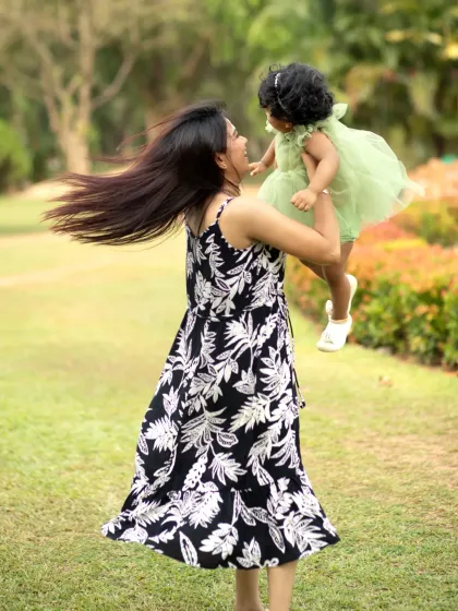 A mother joyfully twirls in a park with her daughter held high in her arms, her hair flying in a beautiful display of motion and happiness.