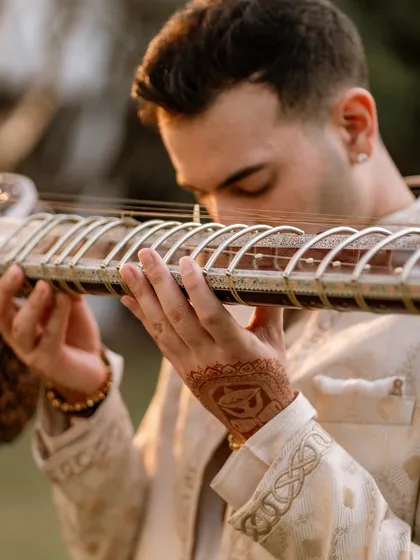 A detailed shot of my hands on the sitar, showing the intricate henna and the craftsmanship of the instrument's frets.