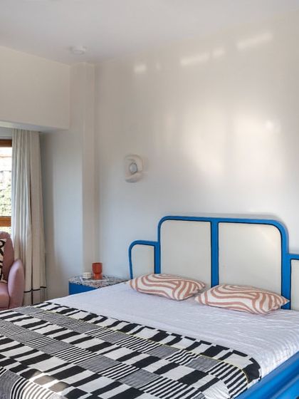 In this bedroom, we played with bold color and form. The custom-designed bed features a striking blue frame with a white headboard, creating a graphic and modern centerpiece. A pink armchair adds a contrasting pop of color.