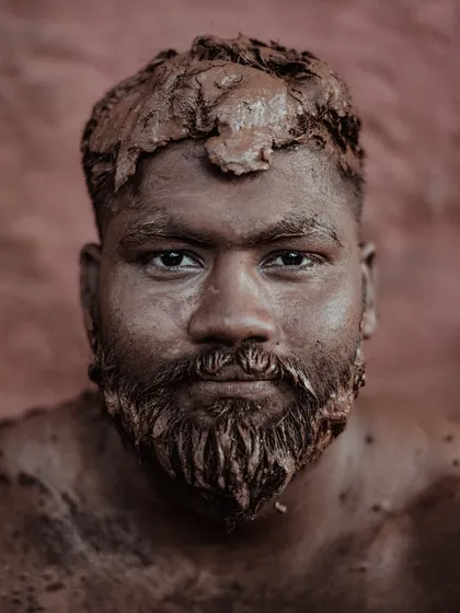 A portrait of a Kushti wrestler from Kolhapur, his face and body covered in the sacred mud of the 'taleem'. His direct gaze speaks of the immense strength, discipline, and tradition inherent in this ancient form of Indian wrestling.
