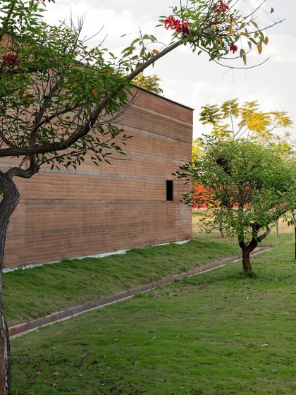 The simple, powerful form of the rammed earth building at the science center, set against a green lawn. The material's natural color comes directly from the local soil.