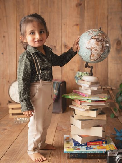 A little scholar and explorer. This toddler is ready to take on the world, posing with a globe and a stack of books.