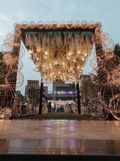 A full view of a fairytale entrance. The combination of a dense green wall, intricate light structures, and a canopy of hanging florals and chandeliers makes a powerful statement.