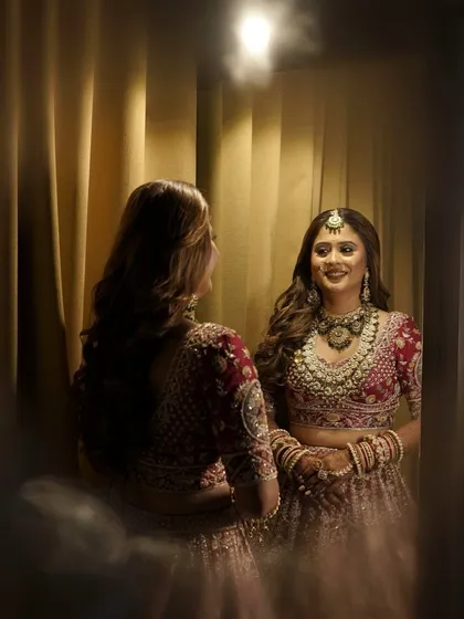 A moment of reflection. The bride looks stunning in her red and gold lehenga, with her hair styled in soft waves and a beautiful jewellery set.