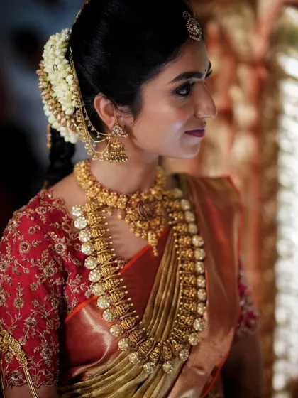 A side profile of the bride, highlighting the heavy embroidery on the sleeve of her red blouse and her traditional temple jewelry.