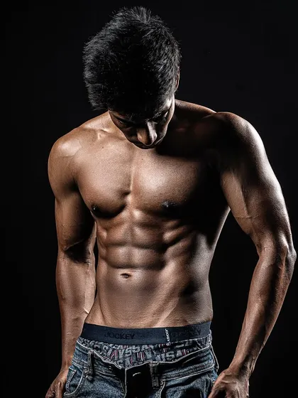 The final result of a successful photoshoot prep. This artistic shot highlights the client's hard-earned abs and lean physique against a dark background.
