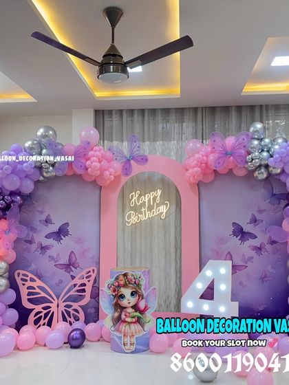 A stunning butterfly theme for a 4th birthday. The setup includes a double-panel backdrop, a pink and purple balloon arch, and large illuminated fairy-light flowers.