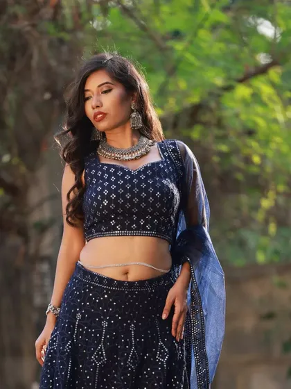A more artistic pose, capturing a moment of serene contemplation. This shot focuses on the mood and the beautiful way the light hits the sequined fabric of the blue lehenga.