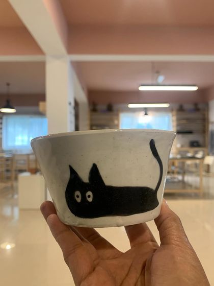 A student's creation, this quirky bowl with a hand-painted black cat, is fresh from the kiln. It's always a joy to see the unique personalities and styles that emerge from our workshops.