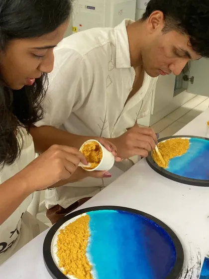 Two participants work together on their resin beach art, adding the sandy texture to the base. My workshops are interactive and perfect for collaboration.