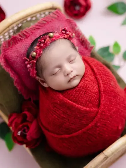 A beautiful newborn surrounded by red roses. The vibrant red wrap and floral elements create a striking and romantic portrait.