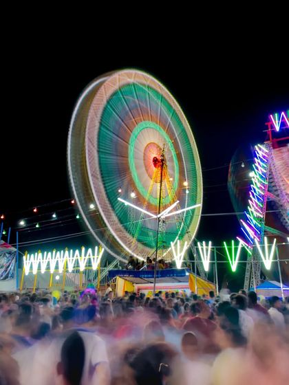 A long-exposure shot of a spinning Ferris wheel at a fair, creating a vibrant circle of light and motion.