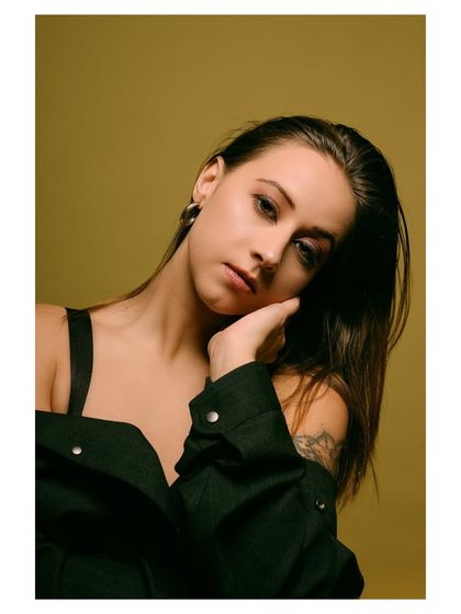 A moody and atmospheric portrait with a dark, edgy feel. The off-the-shoulder jacket and the model's intense gaze create a powerful and mysterious image.