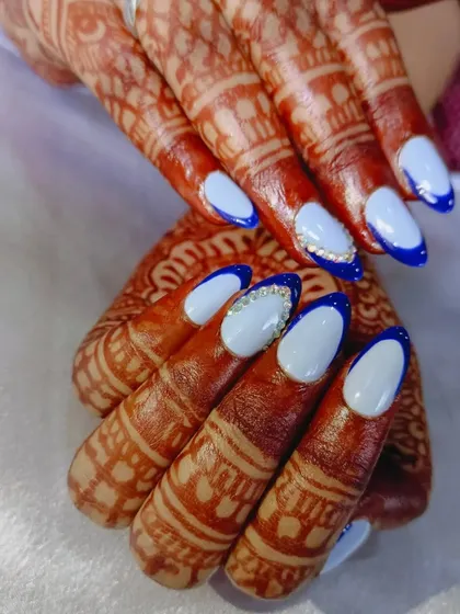 A beautiful bridal set featuring light blue nails with a dark blue French tip outline and rhinestone accents. The color provides a lovely contrast with the warm tones of the henna.