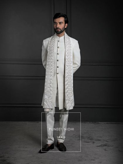 Every weave of this ivory sherwani tells a story of devotion. Handloom silk crafted with patience, a paisley stole shimmering in gold and silver, and metallic buttons that bind it all in quiet majesty.