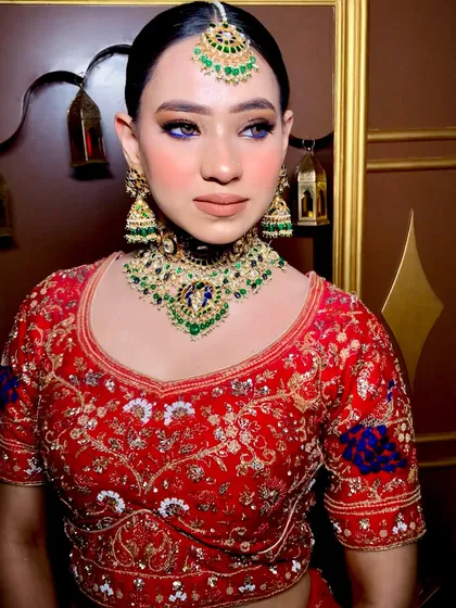 This bride is the definition of elegance in her red lehenga, styled with a heavy polki and emerald jewelry set. The purple pop on the eyes adds a modern twist.