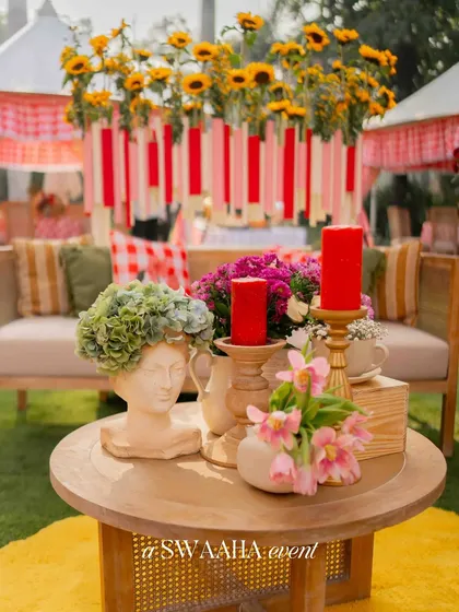 A close-up of a table centerpiece from the picnic-themed baby shower, featuring a classical bust with a floral crown, red candles, and fresh sunflowers.