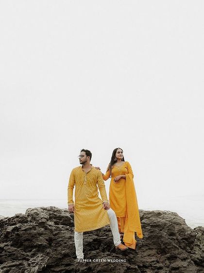 A wide, dramatic shot of the couple on the rocks against the expansive sea, creating a powerful and epic pre-wedding portrait.