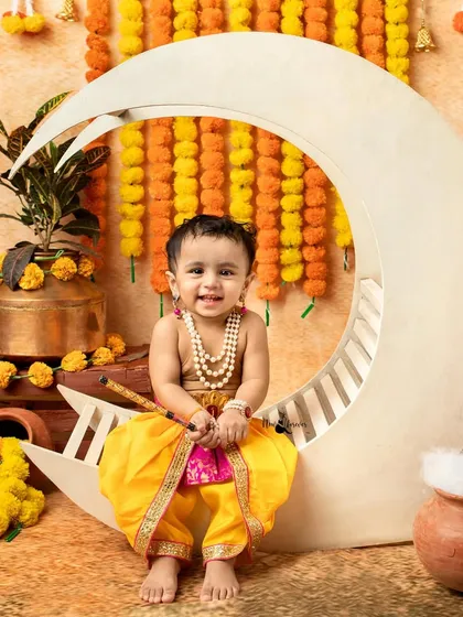 A happy little Krishna sitting on the moon prop, ready to play his flute. The bright smile makes this a heartwarming shot.