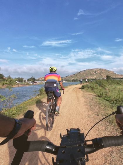A first-person view of the Devanahalli Heritage Ride, cycling on a dirt path alongside a lake with hills in the background. It's history surrounded by nature.