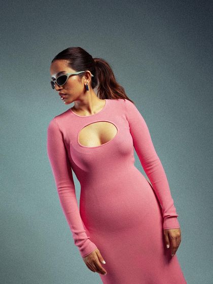 A composed and elegant studio portrait. The model's pose highlights the long sleeves and form-fitting shape of the pink dress, creating a sophisticated and modern look.