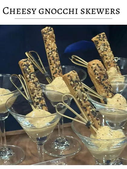 Cheesy gnocchi skewers served in a martini glass. The soft, pillowy gnocchi is paired with a creamy cheese sauce and a sesame breadstick for dipping.