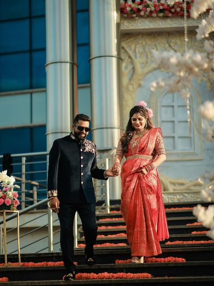 A stylish couple making their entrance down a staircase decorated with marigolds for their pre-wedding event.