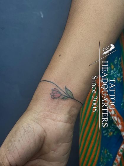 A delicate wristband tattoo of a single line with a small, simple flower, combining minimalist and nature themes.