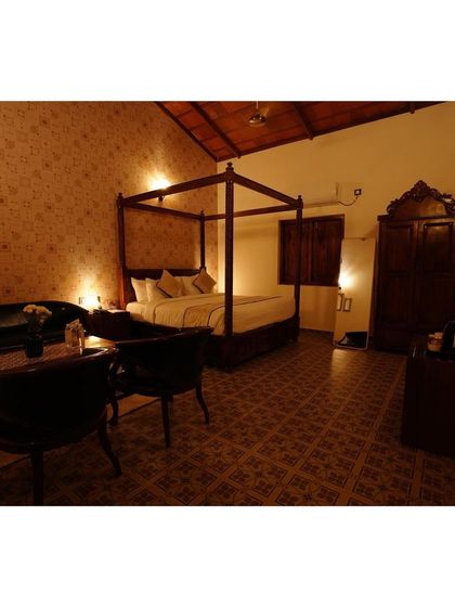 This spacious suite at the resort features classic dark wood furniture, including a four-poster bed and a large armoire. The patterned floor tiles and warm lighting create a sense of old-world elegance and comfort.