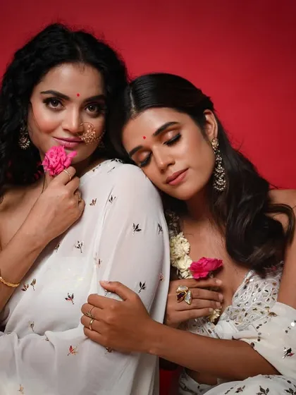 This image has a soft, romantic feel. The models are styled with minimal jewellery and fresh flowers, letting the beauty of the sarees and their connection be the focus.