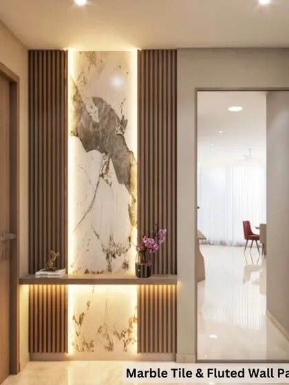 See how beautifully different materials can come together. This entryway design combines the elegance of a large marble tile with the texture of wooden fluted wall panels, all highlighted with soft backlighting for a warm and welcoming feel.