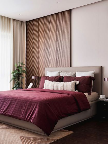 The guest bedroom features a beautiful chevron-patterned wood headboard that adds texture and warmth. The rich burgundy bedding creates a cozy and inviting feel for visitors.
