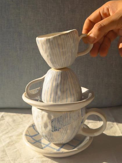 A stack of beautifully crafted cups and saucers made using hand-building techniques. The subtle textures and patterns show the artist's touch.