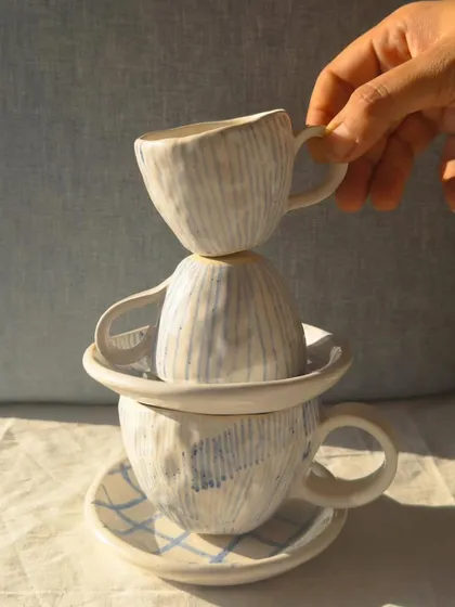 A stack of beautifully crafted cups and saucers made using hand-building techniques. The subtle textures and patterns show the artist's touch.