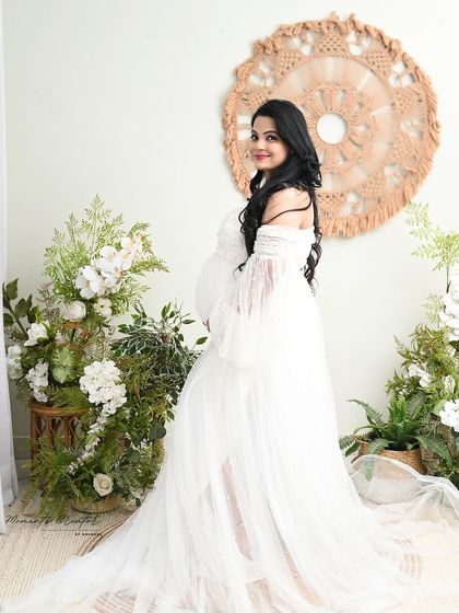 A radiant smile in the boho-floral setup. This portrait captures the pure joy and beauty of the mom-to-be in a classic white gown.