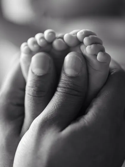 A powerful black and white macro shot of a parent's thumbs cradling their baby's feet.