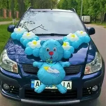 A cute car decoration for a baby's arrival, featuring a large teddy bear foil balloon on the car's bonnet.