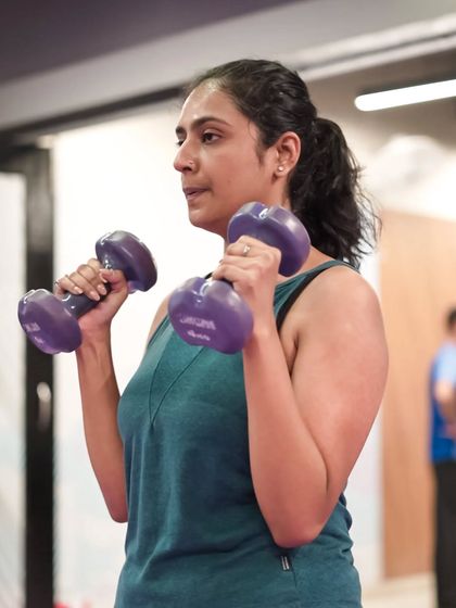 A member performs bicep curls with purple dumbbells, focusing on isolating the bicep muscles for strength and toning.