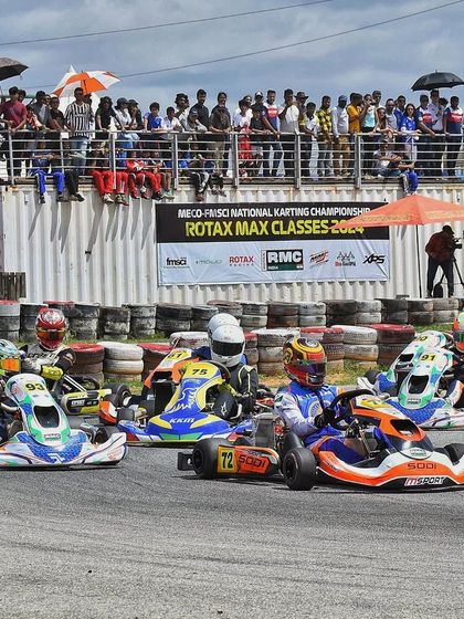 A pack of karts navigates a corner under the watchful eyes of spectators.