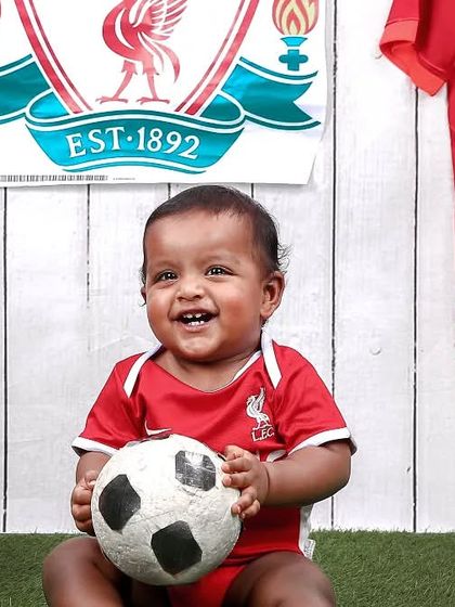 For the football fans in the family! This little one is showing his team spirit in a Liverpool FC themed setup, complete with the jersey and a soccer ball.