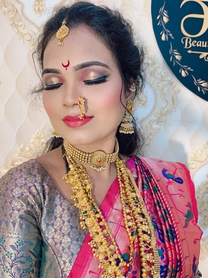 A close-up of a Maharashtrian bride. The makeup features a golden shimmer on the eyelids, a classic red bindi with a crescent moon design, and traditional gold jewelry.