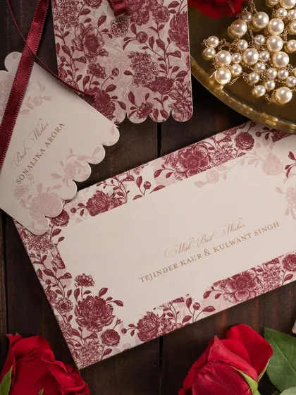 A rustic and romantic flat lay of a floral wedding invitation suite. The styling with a ribbon, pearls, and roses on a wooden background creates a warm and inviting feel.