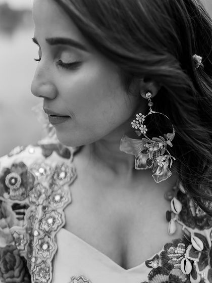 A black and white close-up of the bride, highlighting her delicate features and the stunning floral statement earrings chosen for her Haldi look.
